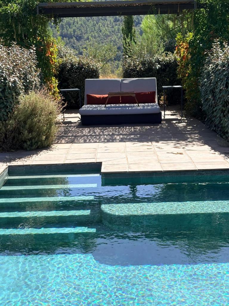 Área de descanso al lado de una piscina, con un sofá acompañado de mesas auxiliares y rodeado de vegetación.