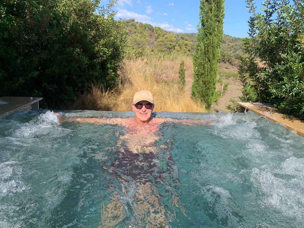 Una persona relajándose en un jacuzzi al aire libre con vegetación y montañas de fondo.