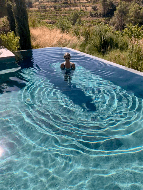 Una persona en una piscina de agua cristalina, creando ondas en la superficie, rodeada de un paisaje natural.