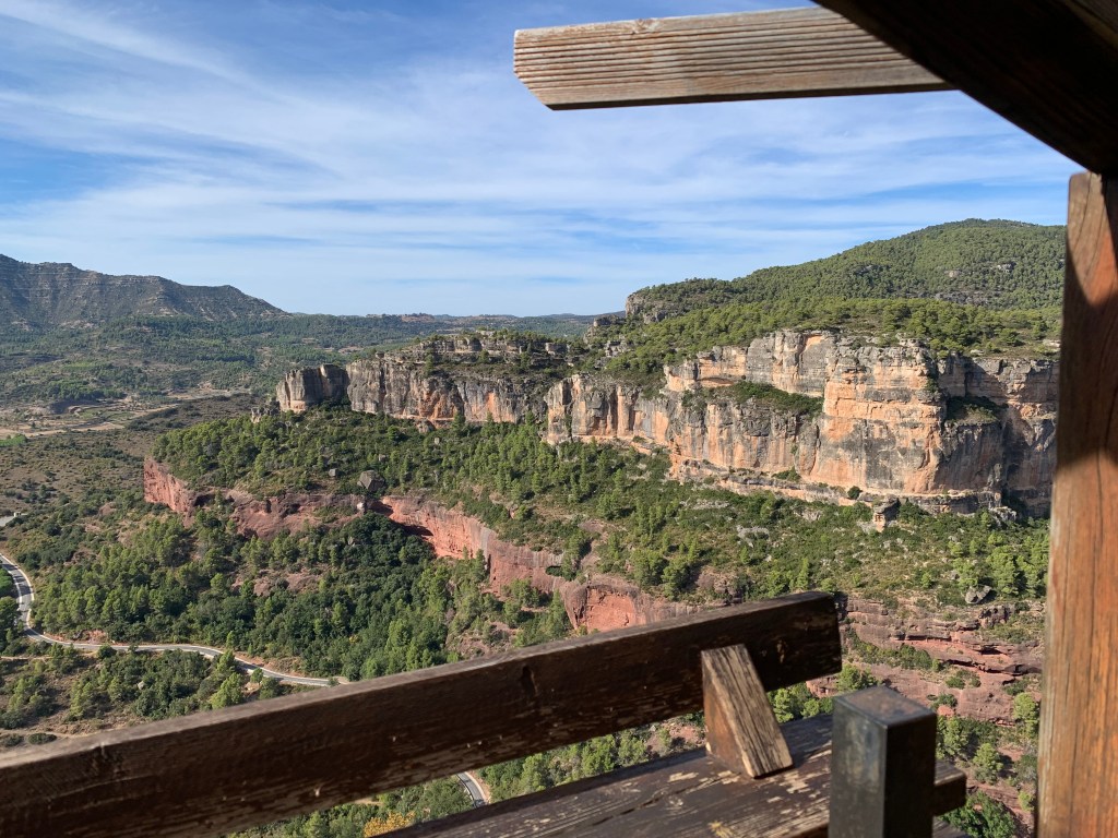Vista panorámica de un paisaje montañoso con acantilados y vegetación densa, capturada desde una estructura de madera.
